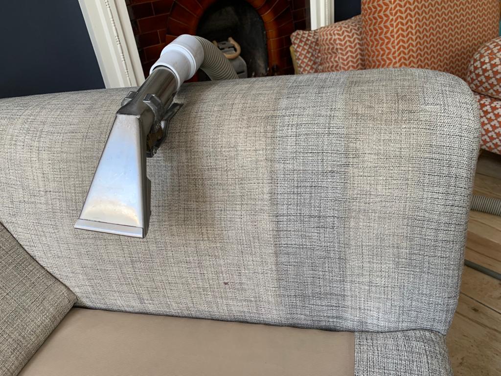 This is a photo of an arm of beige sofa that shows a test patch that has been steam cleaned. The steam cleaning machine is also showing in the photo works carried out by Blackheath Carpet Cleaning.