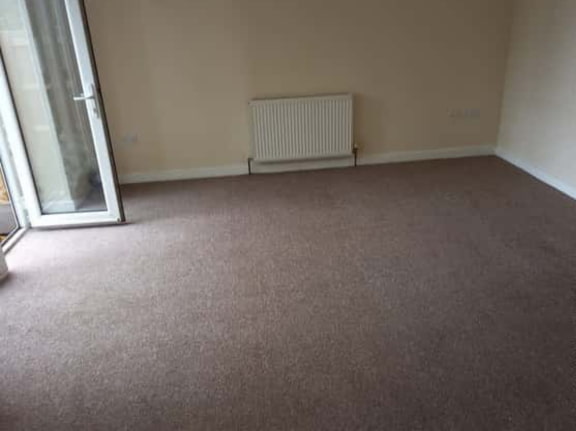 This is a photo of a living room after it has been cleaned. The room is empty and has a brown carpet that has been steam cleaned carried out by Blackheath Carpet Cleaning.